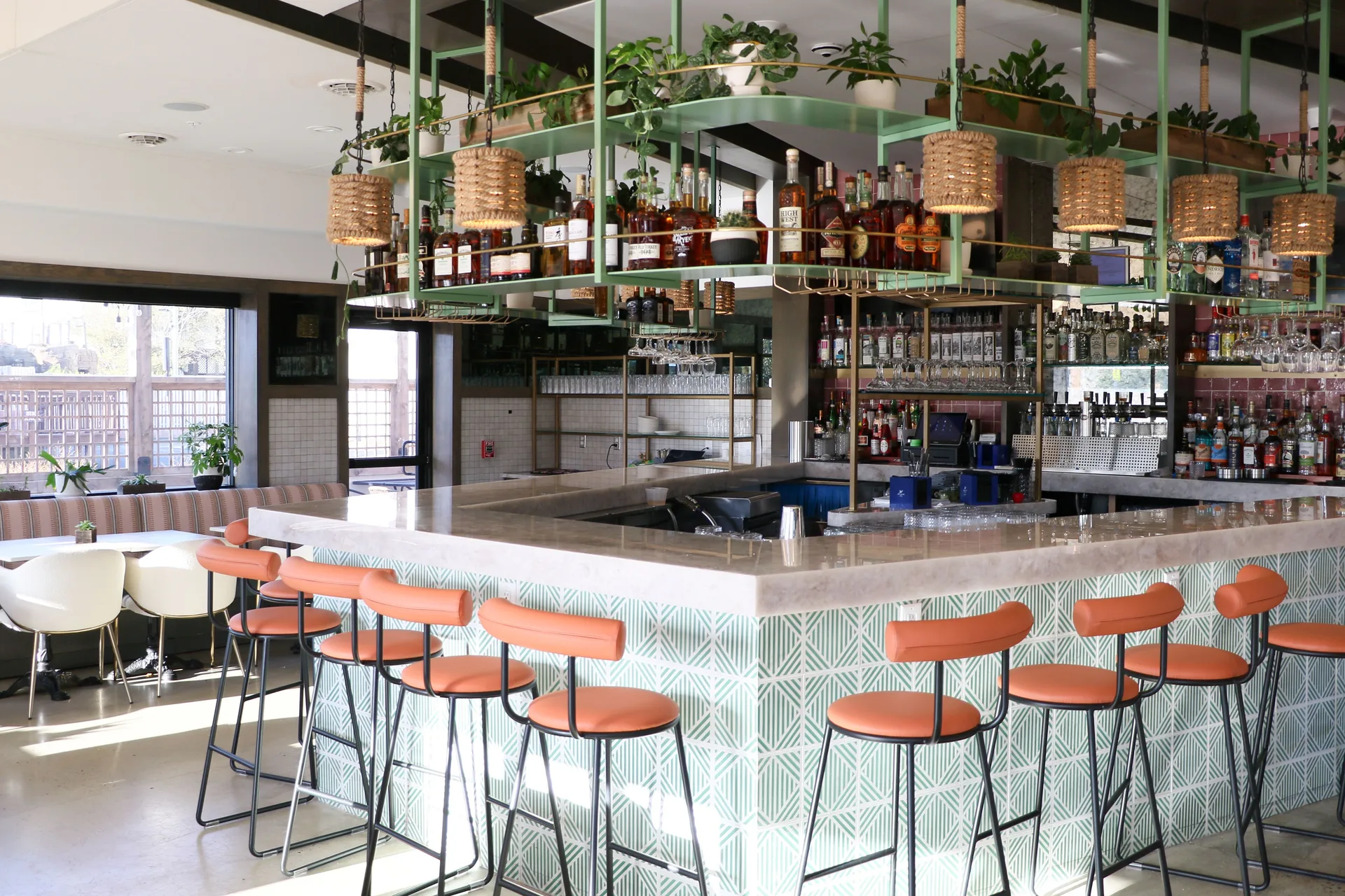 The inside of a restaurant with a view of the bar with orange bar seats surrounding the bar.