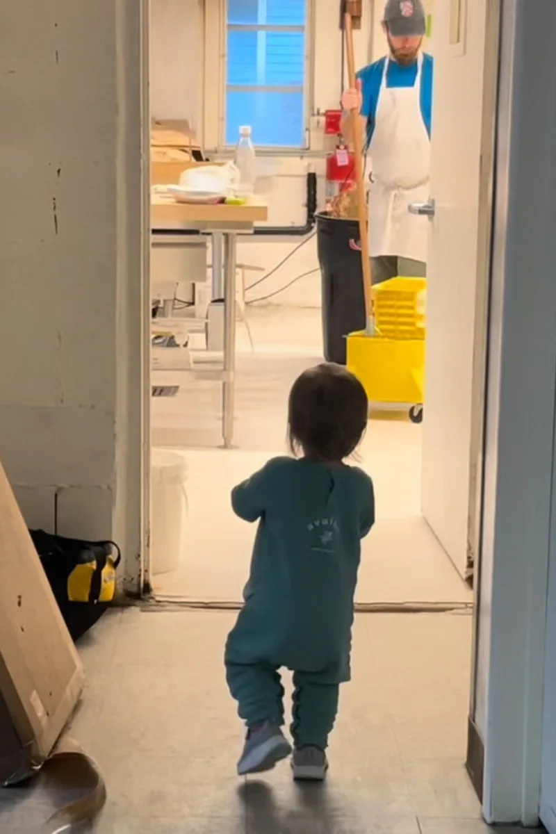 A baby walking down a hallway at a bakery.