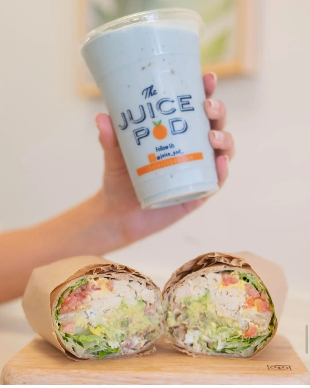 A hand holding a white smoothie above a wrap cut in half. 
