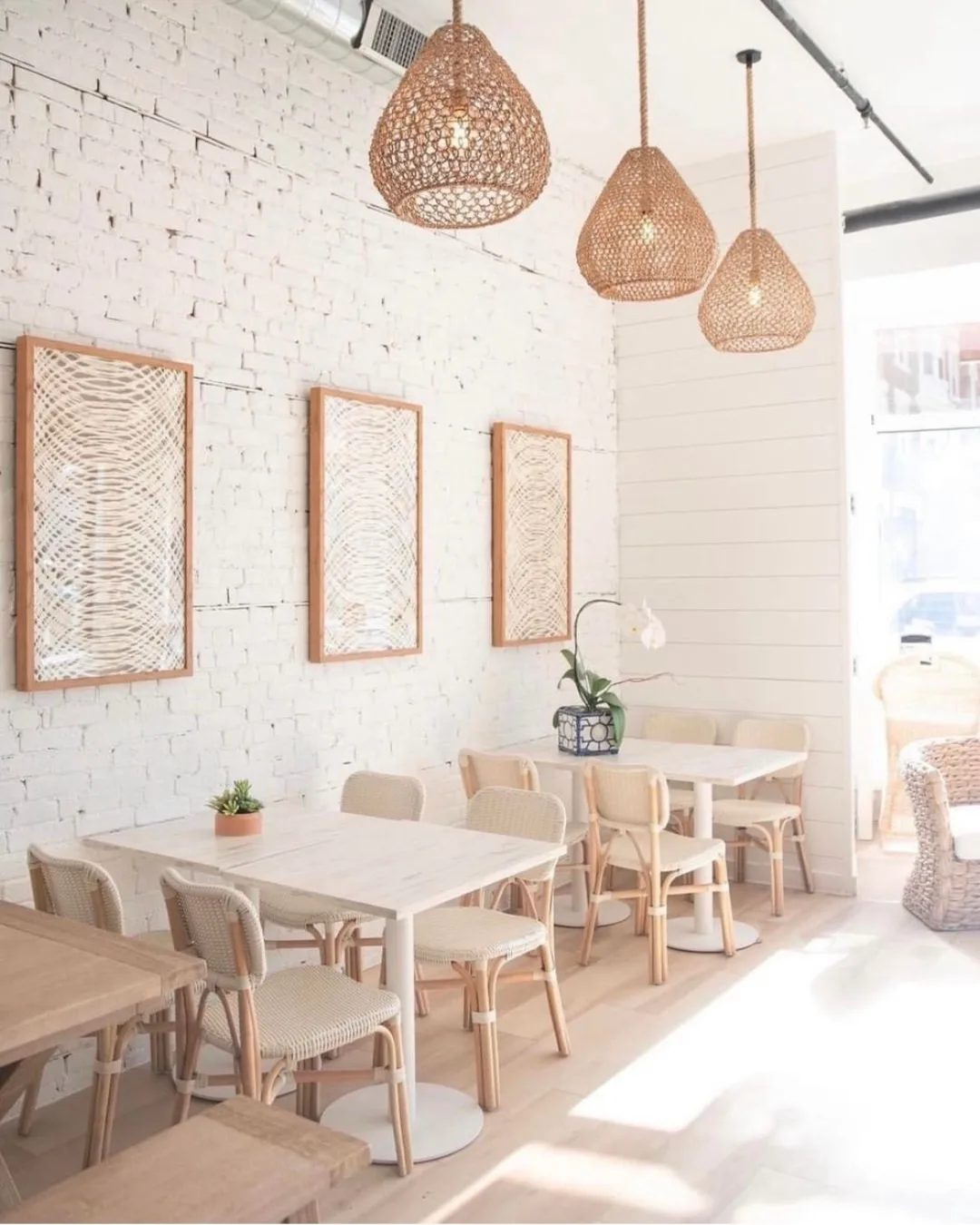 An empty restaurant with white tables, and brown hanging lighting. 