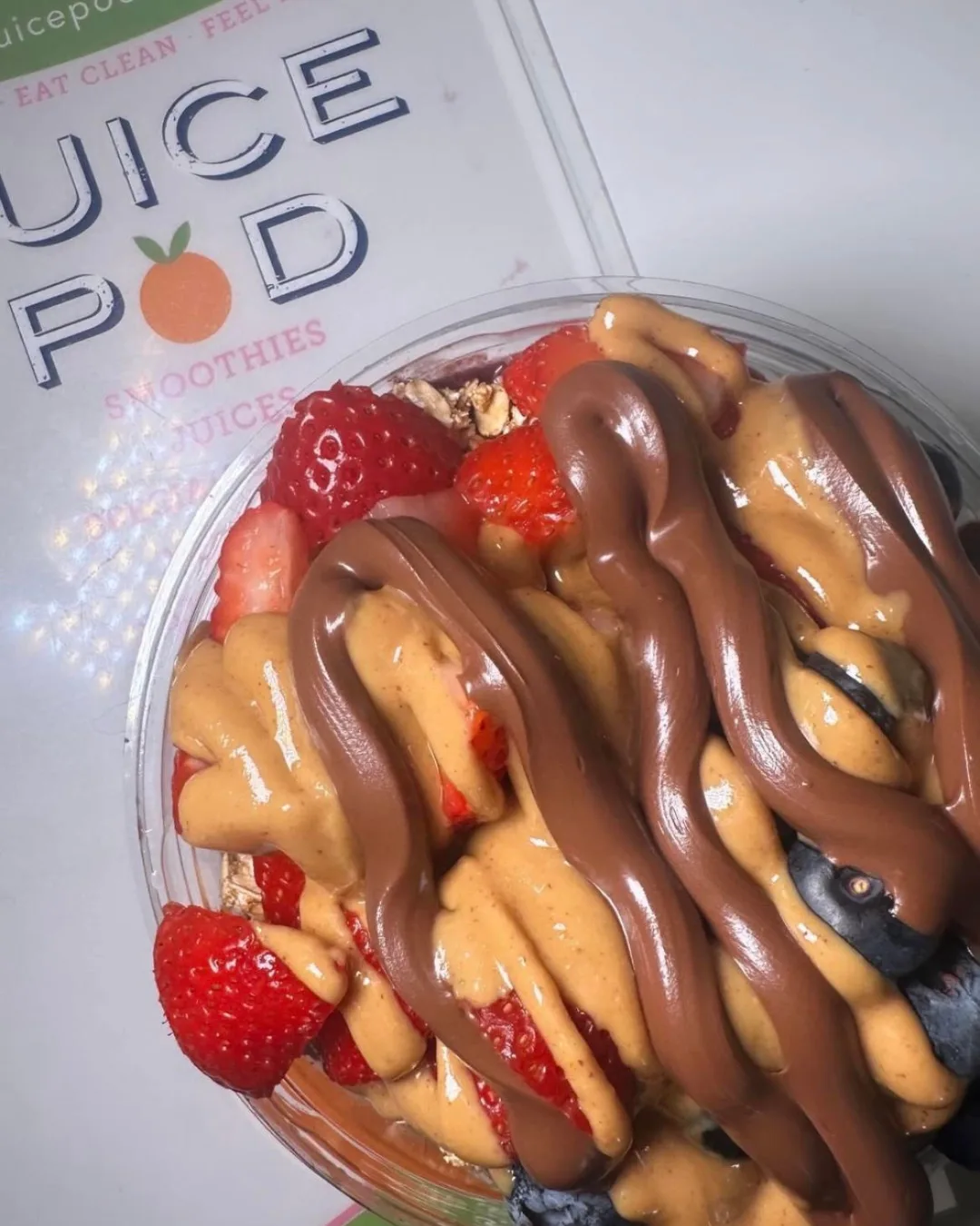 A menu from The Juice Pod underneath an acai bowl featuring bananas and peanut butter.